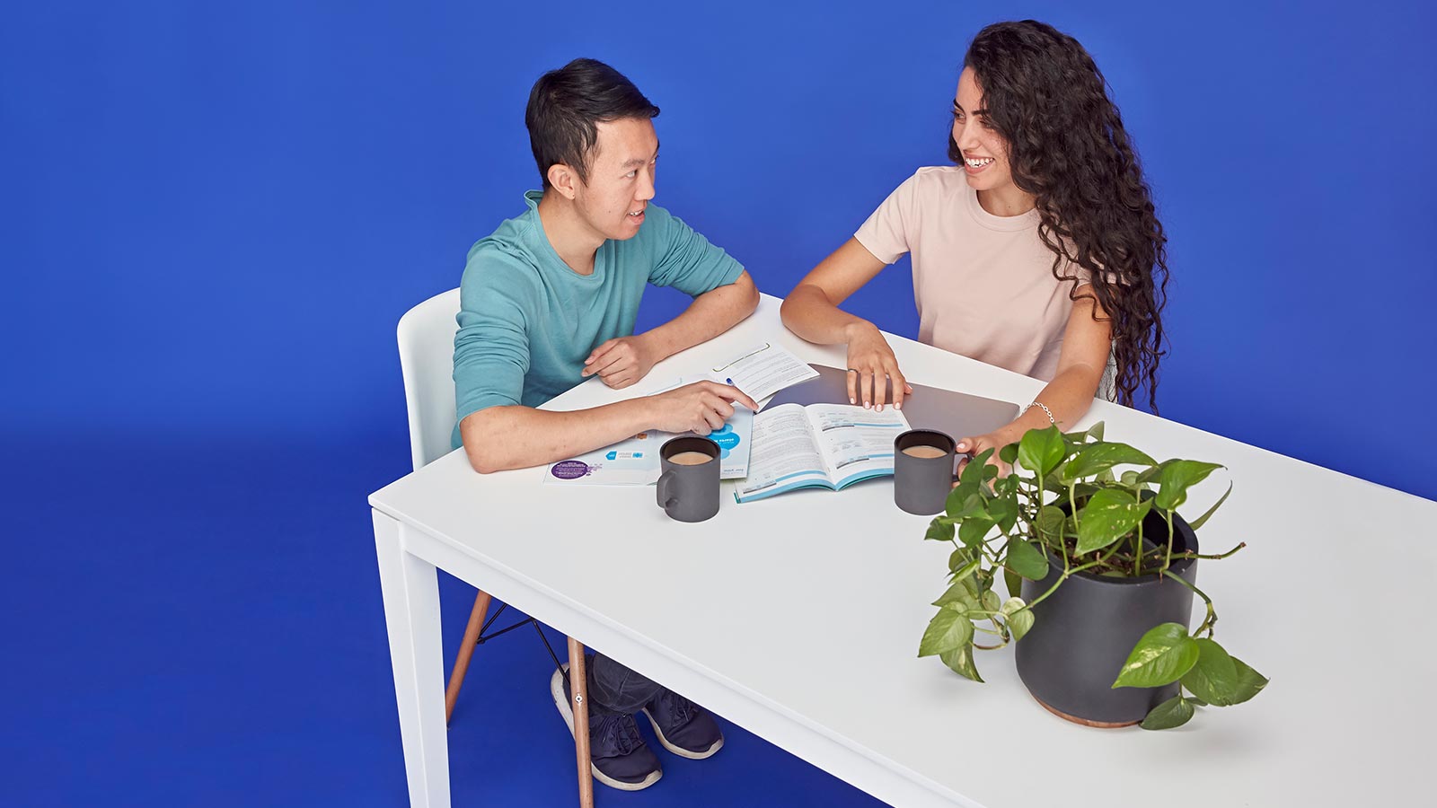 Couple sitting at a table reading a booklet, drinking coffee.