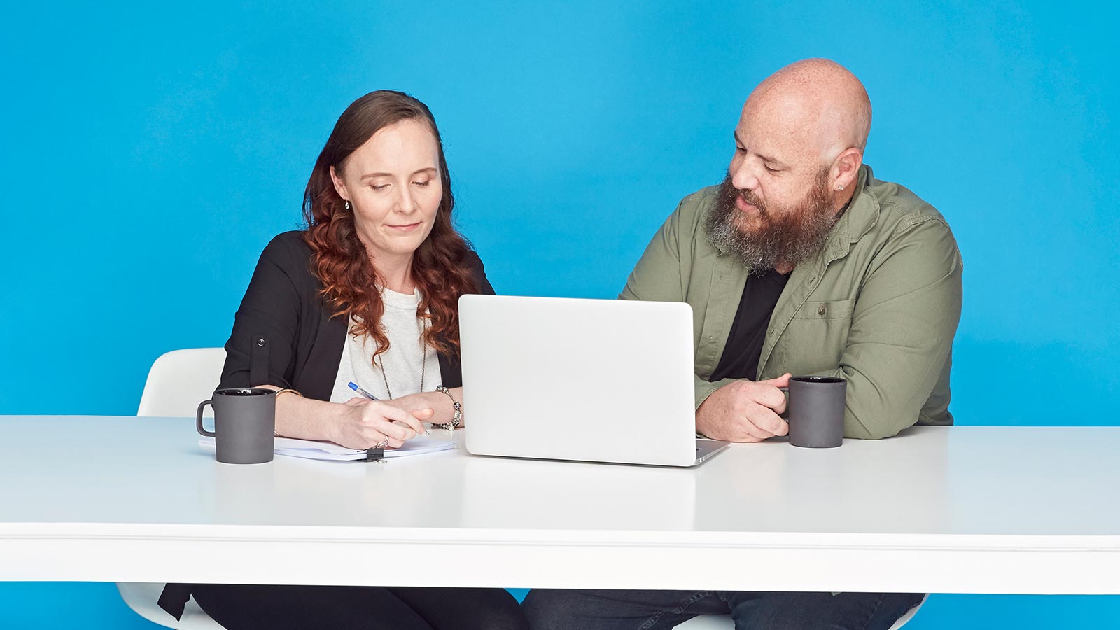 Couple sitting in front of a laptop, drinking coffee.