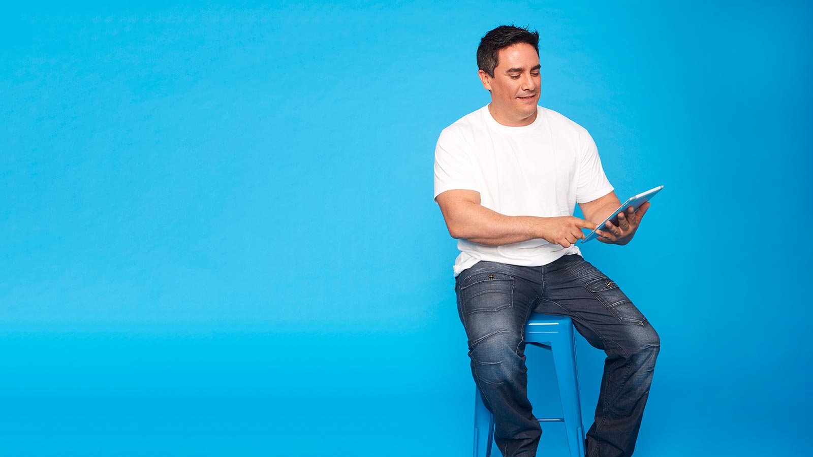 Man sitting on stool holding tablet.