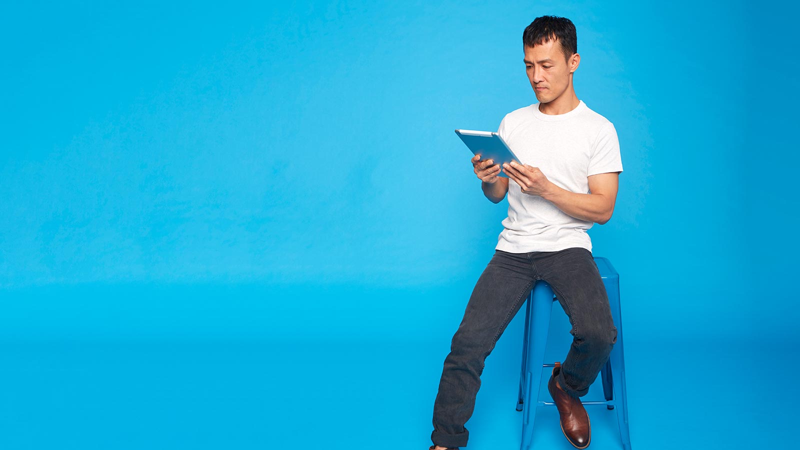 Man sitting on a stool, holding a tablet.
